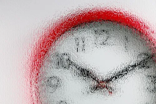 A red wall clock behind heavily blurred, frosted glass.